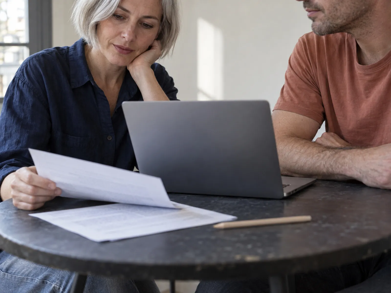 Two people reading a printed document across a table with a laptop