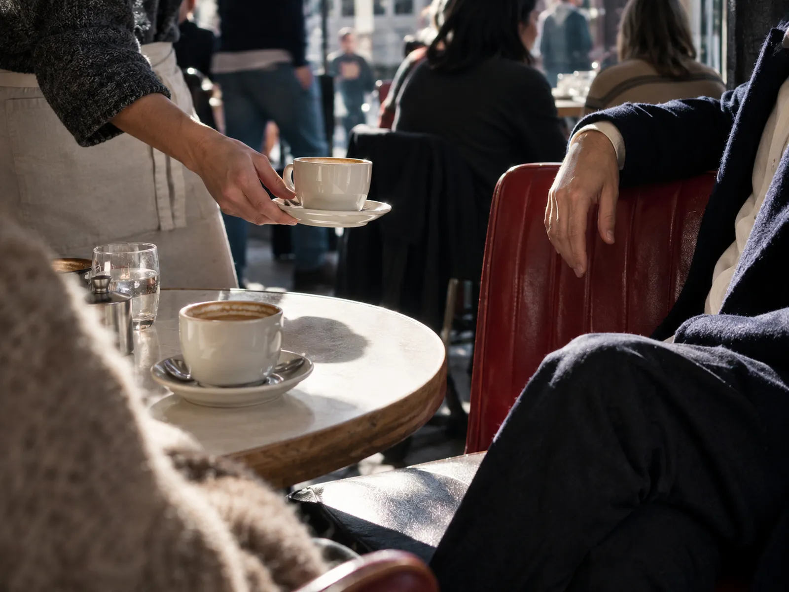A server bringing a coffee to a table in a busy café